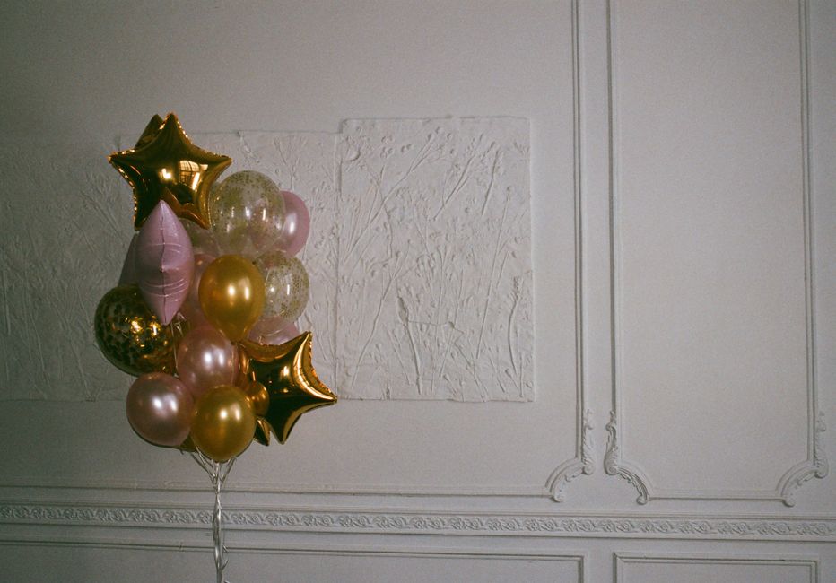 A cluster of helium-filled balloons arranged in a bouquet, featuring metallic gold, soft pink, and transparent designs with confetti and leopard print patterns, some shaped as stars, all tied together