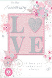 This anniversary card is depicted as delicately romantic, with a design that feels as gentle as an evening stroll along the leafy streets of Addlestone. At the centre, the word LOVE stands out in bold, raised letters, as if carefully embossed onto the card. The letters are generously coated in fine blush-pink glitter, infused with hints of pearlescent white and silver, so that they catch and scatter light with soft, refined sparkle. The textured surface suggests both visual and tactile richness, inviting fingers to linger on each curving stroke. Behind the central word, the background fades from a warm, powdery pink at the heart to a pale, almost white tone toward the edges, giving the design a subtle halo effect. Encircling and framing the word LOVE, a collection of stylised flowers, slender leaves, and delicate vines spirals across the card's face. Drawn in fine lines of soft grey, blush, and muted mauve, and accented with restrained touches of silver, these blossoms appear almost like a florist's pencil sketches for an anniversary bouquet destined for a home near Addlestone Moor. The floral elements move in graceful arcs, echoing the natural curves of stems in a hand-tied arrangement, while smaller sprigs, buds, and curled flourishes fill gaps with gentle rhythm. The card's heartfelt anniversary greeting is written in an elegant script, its looping letters harmonising with the shape of the vines and petals, giving the text the same sense of movement as the flowers themselves. Altogether, the card conveys tenderness, trust, and enduring affection - a paper tribute to long-lasting love that pairs beautifully with a fresh, romantic bouquet delivered across Addlestone and the surrounding neighbourhoods.